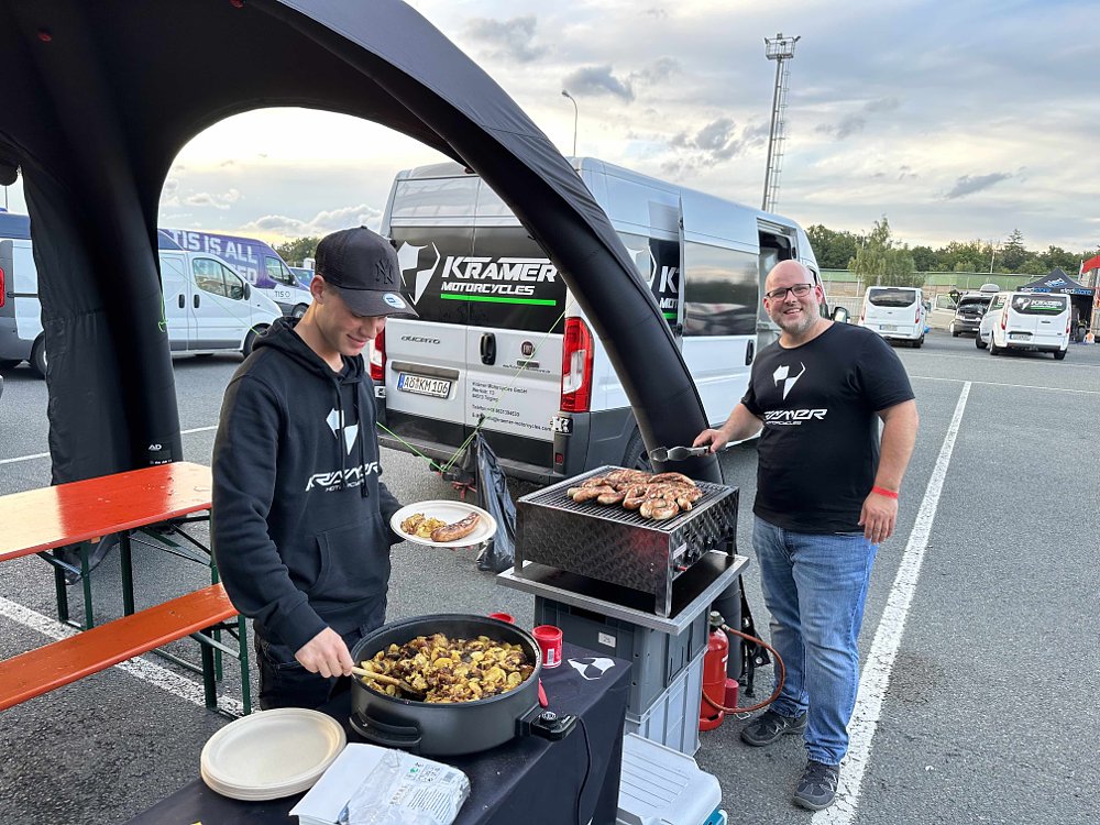 Two men stand at a barbecue serving food in the paddock of the Brno Circuit in the Czech Republic.
