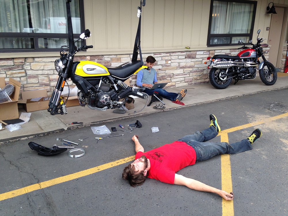 Zack lying flat on the ground as a motorcycle hangs from straps behind him
