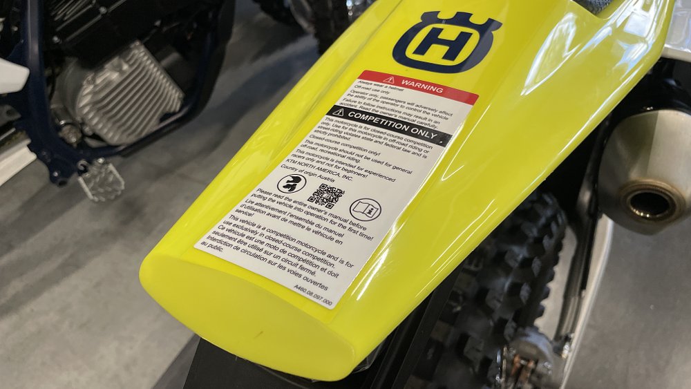 On the tail section of a Husqvarna dirt bike, there is a warning label that has language stating the motorcycle is for competition use