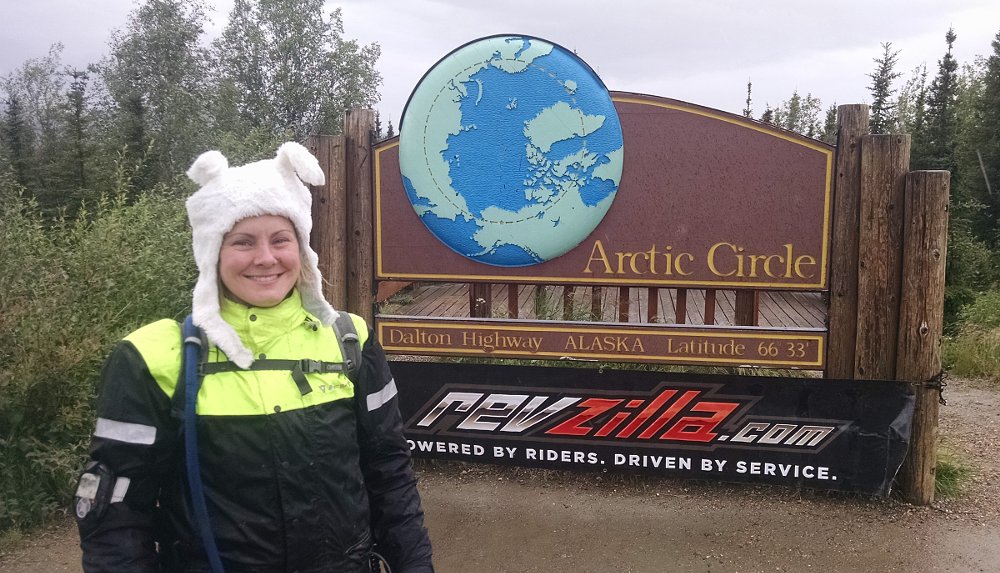 Kate Johnston posing in front of the sign marking the Arctic Circle in Alaska