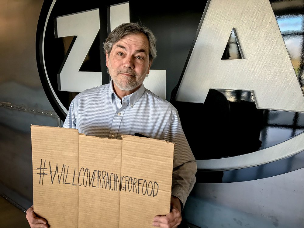 Lance holding a cardboard sign saying '#willcoverracingforfood'
