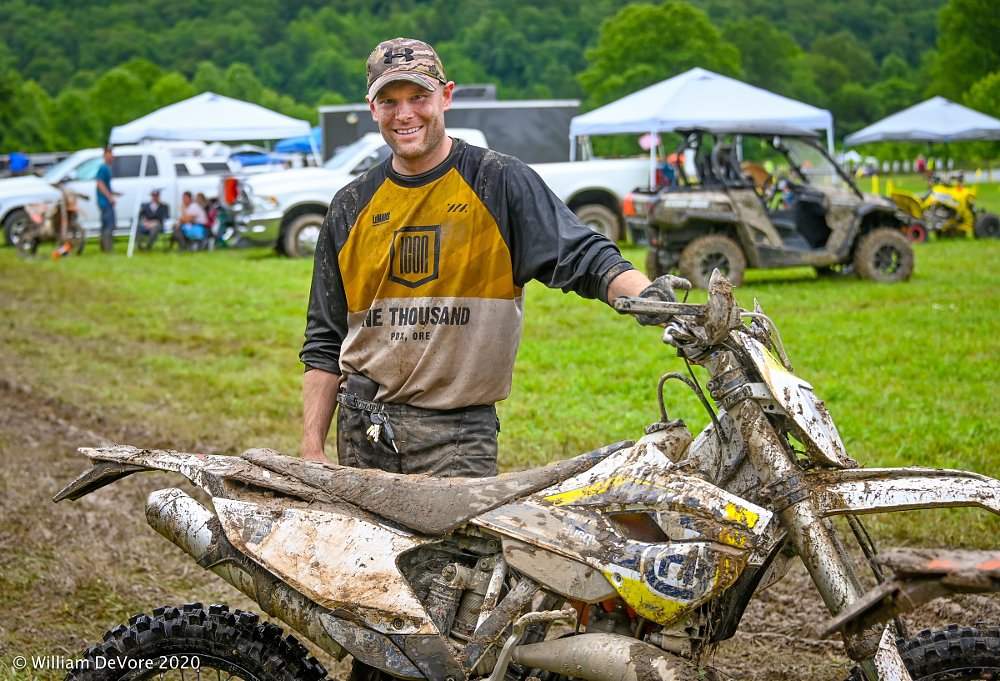 Drew Faulkner covered in dirt, smiling and posing with his off-road Husqvarna motorcycle
