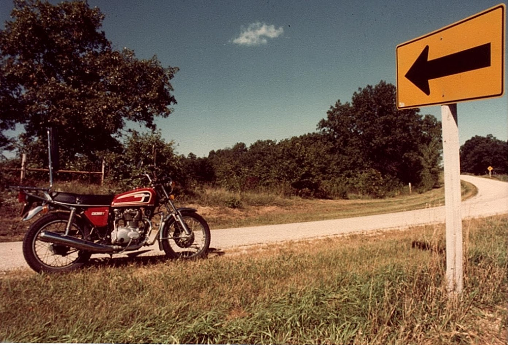 Honda CB360T on a country road by a curve sign