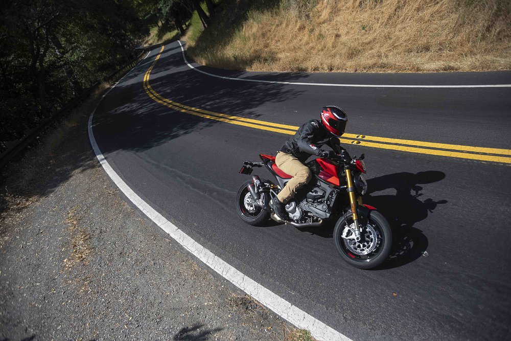 A 2024 Ducati Monster SP rides down a two-lane road through the forest in Corte Madera, CA.