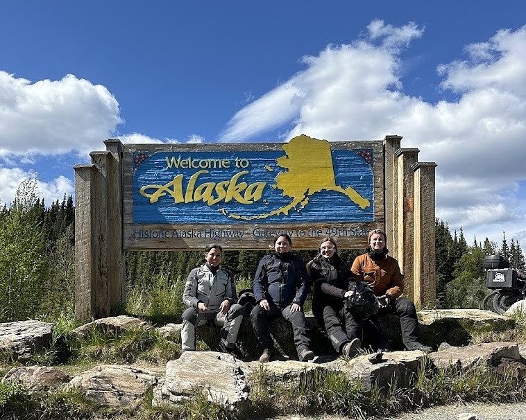the four riders in front of the sign marking the Alaska border