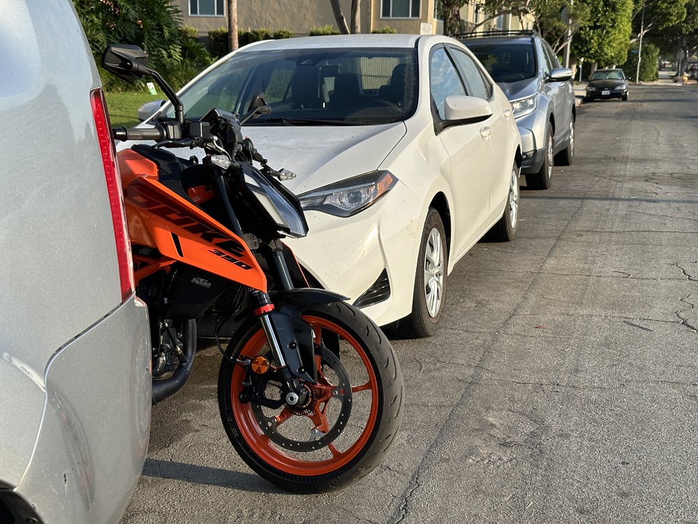 2024 KTM 390 Duke parked between cars on a street.