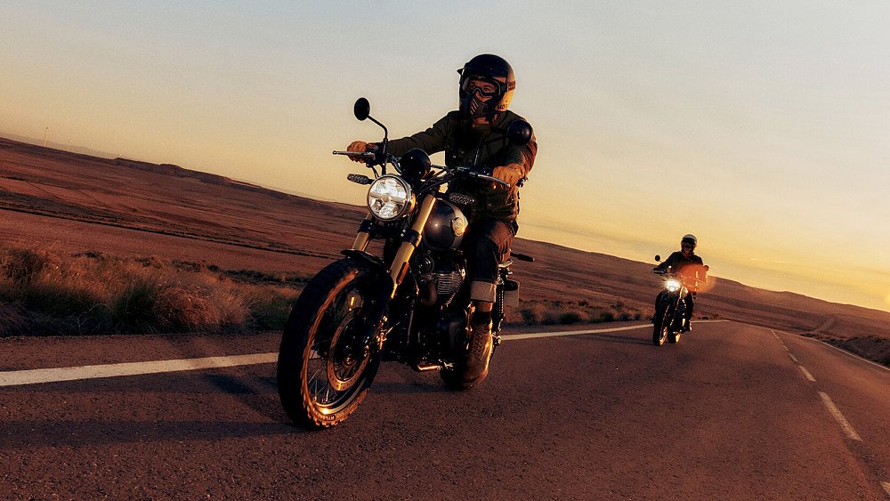 Two Royal Enfield Bear 650s roll down a desert highway with the sun setting in the background.