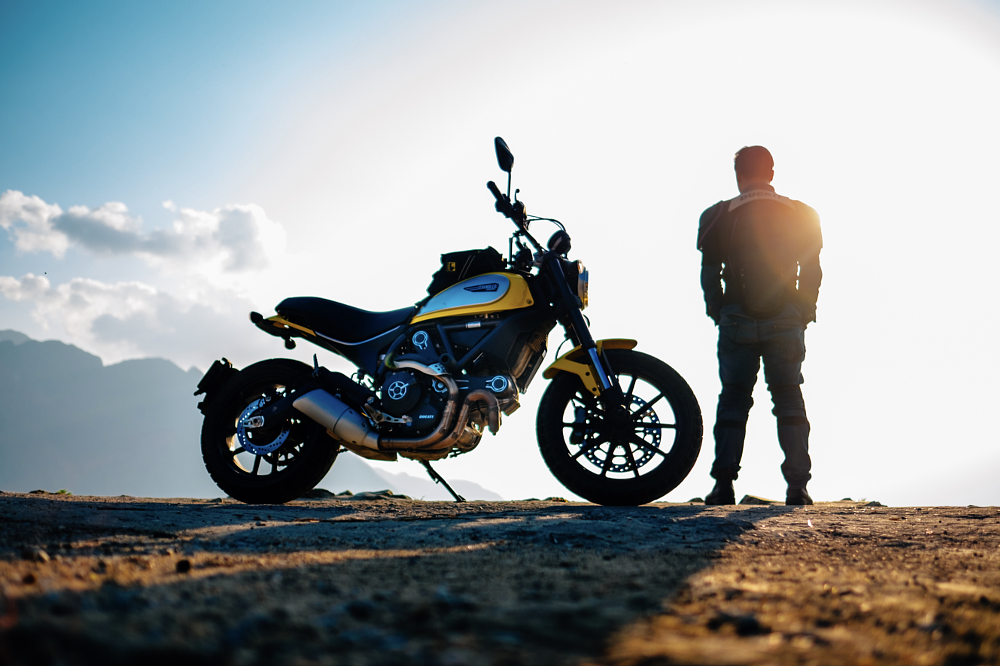 rider standing by motorcycle and looking at the sunset