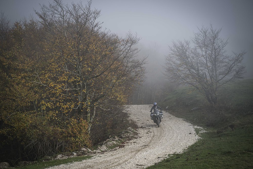 Dustin riding a Ducati Multistrada on a dirt road through a misty mountain forest