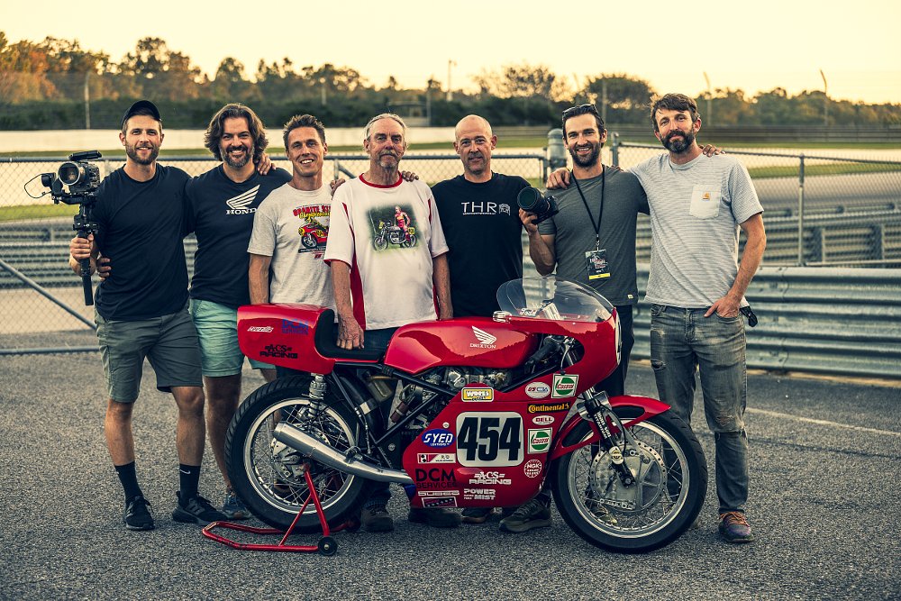 Ari and the rest of the CTXP film crew posed with a red vintage racing motorcycle
