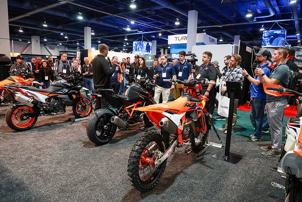 A group of motorcycle industry members surround an KTM exhibit.
