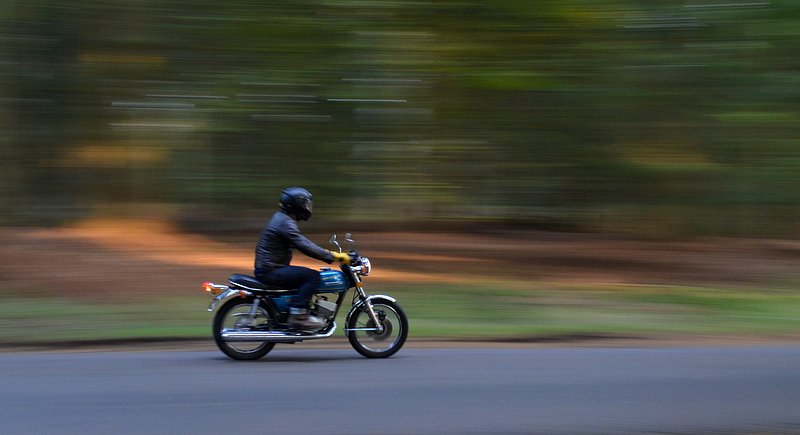 riding the blue Suzuki GT250 on a country lane, blurred background