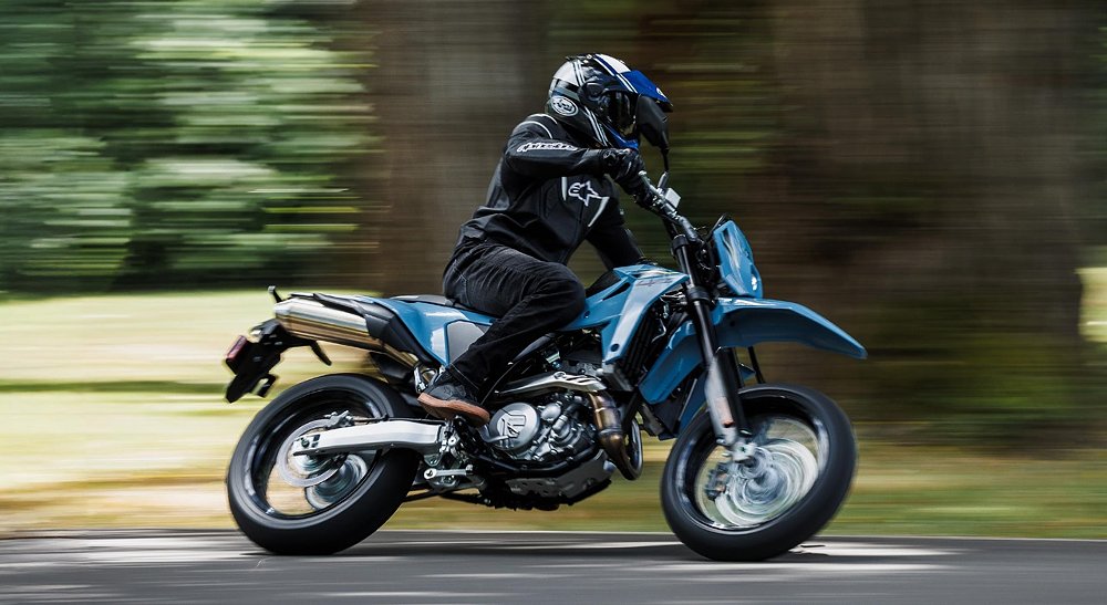 A DR-Z4SM rider blasts through a corner on a heavily forested road.