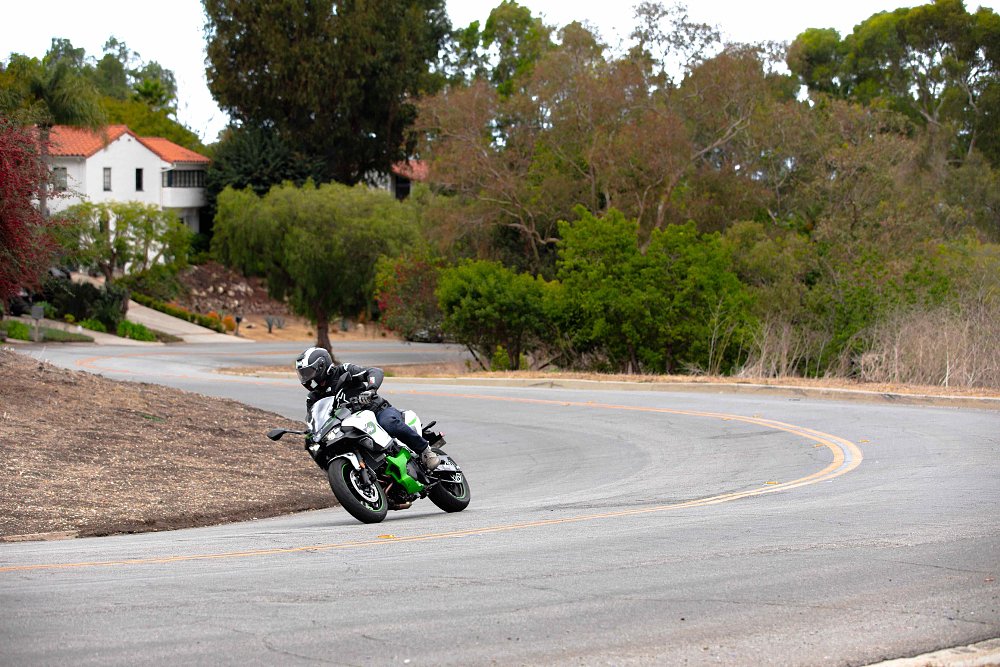 2025 Kawasaki Ninja 7 Hybrid riding through a rural curve with a house in the background.
