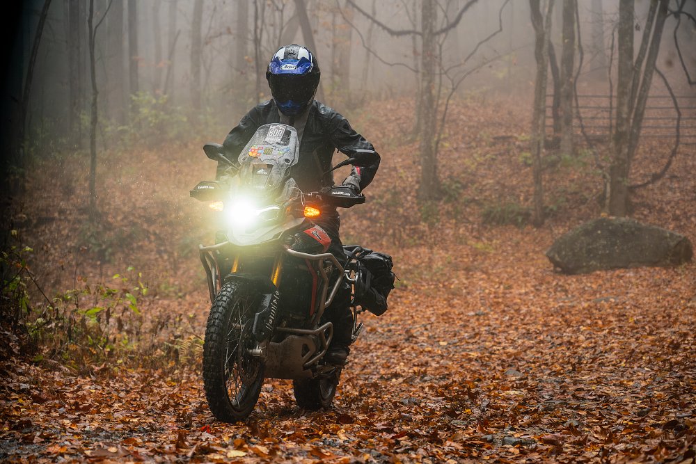 Dustin riding the Tiger 900 Rally Pro over a leaf-covered trail in the rain.