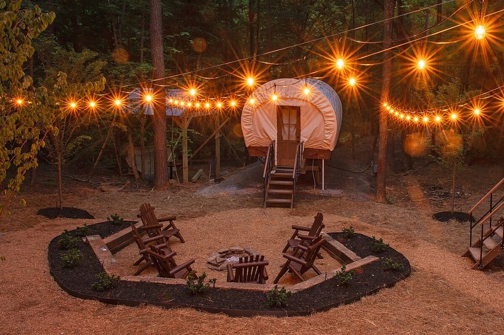 A view of the Welcome Valley Village campground, with a Conestoga wagon in the background and a fire pit in the foreground.