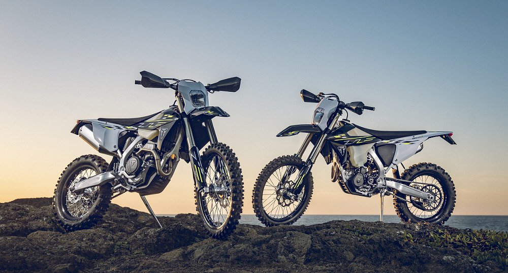 the two enduro motorcycles parked atop rocks in front of the ocean