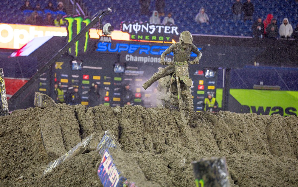 motocross racer atop a jump in the deep mud, trying to catch his balance, steam coming from his engine