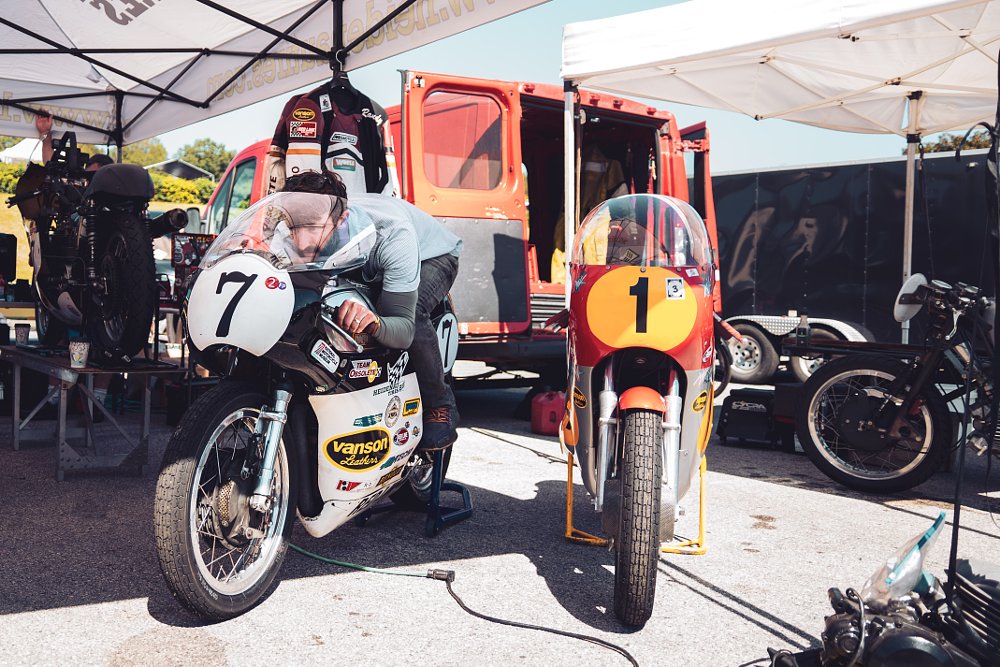An AJS 7R sitting next to a three-cylinder MV Agusta GP in the Barber Motorsports Park paddock.