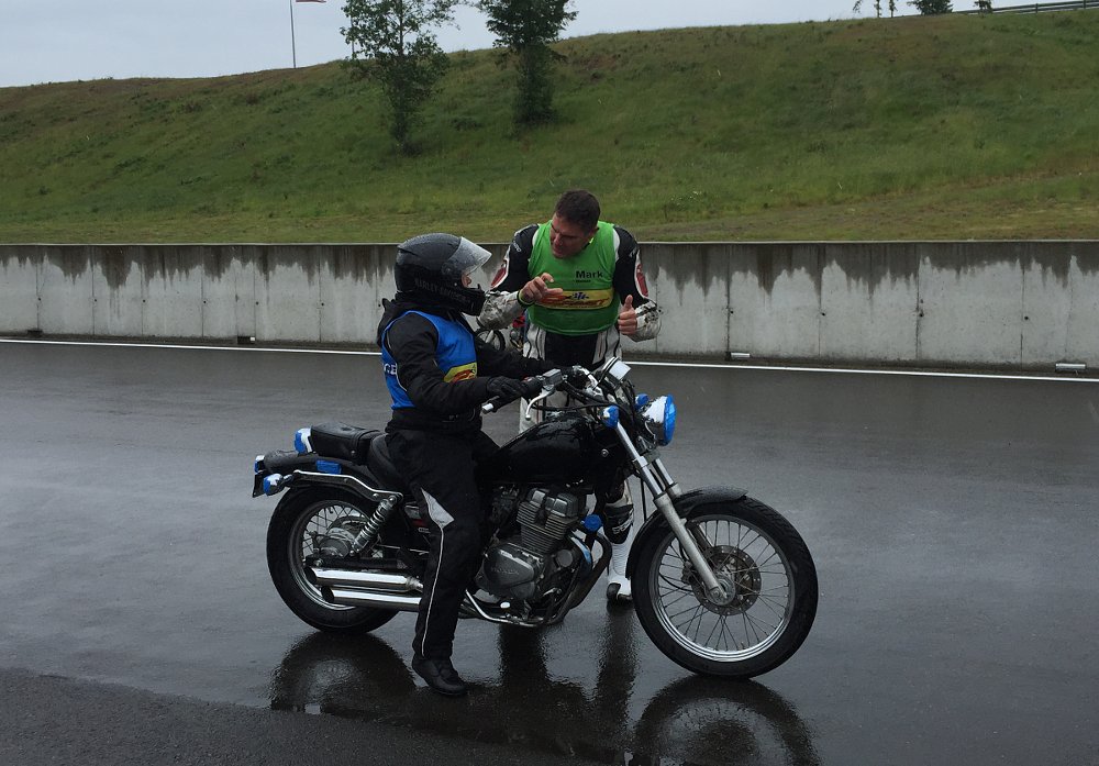 instructor explaining a braking drill to a woman rider on a small motorcycle on wet pavement
