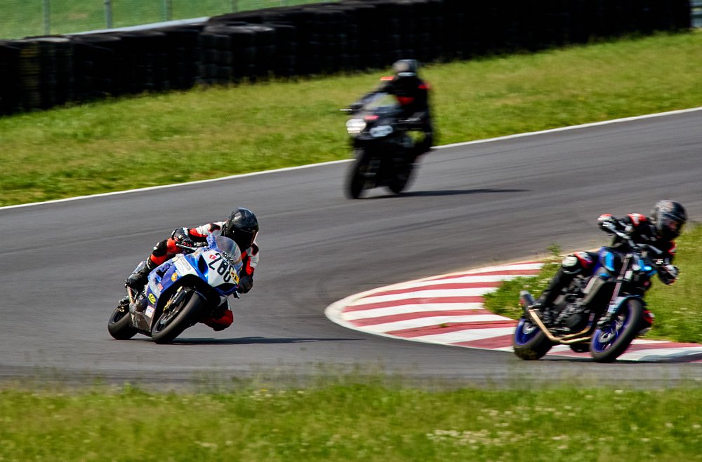 riders on a sport-touring motorcycle, a sport bike, and a cruiser go through a corner on a race track at a track day
