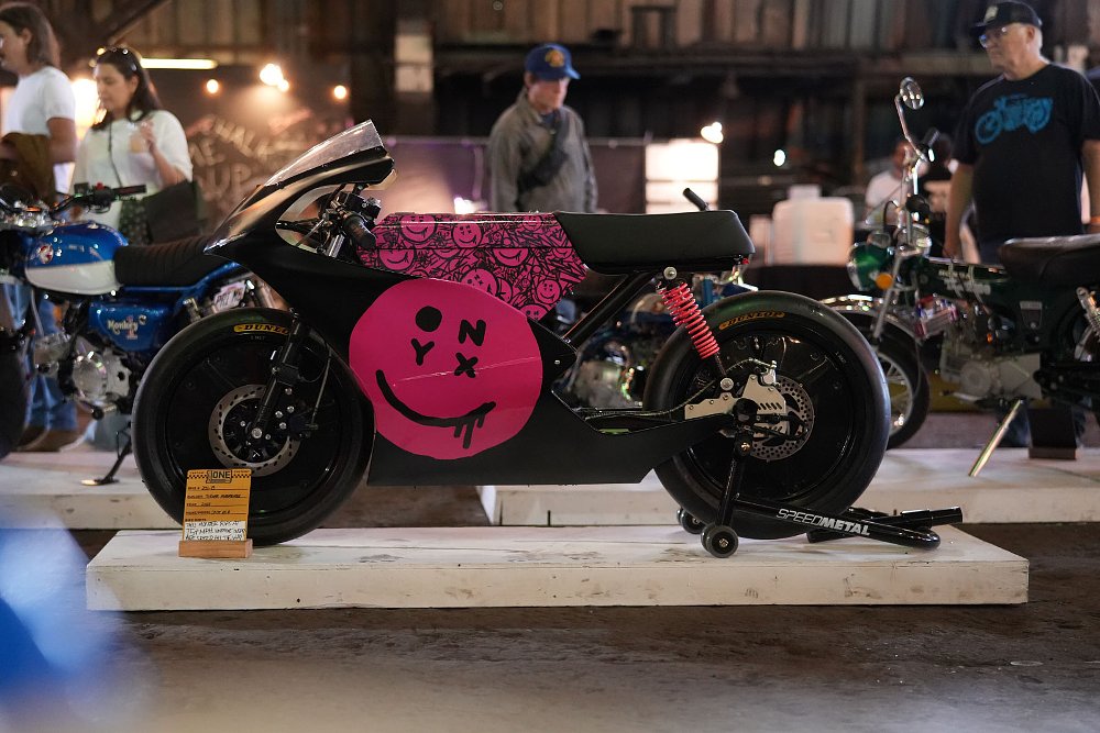small electric race motorcycle with pink smiley face design on the bodywork on a pedestal at the show