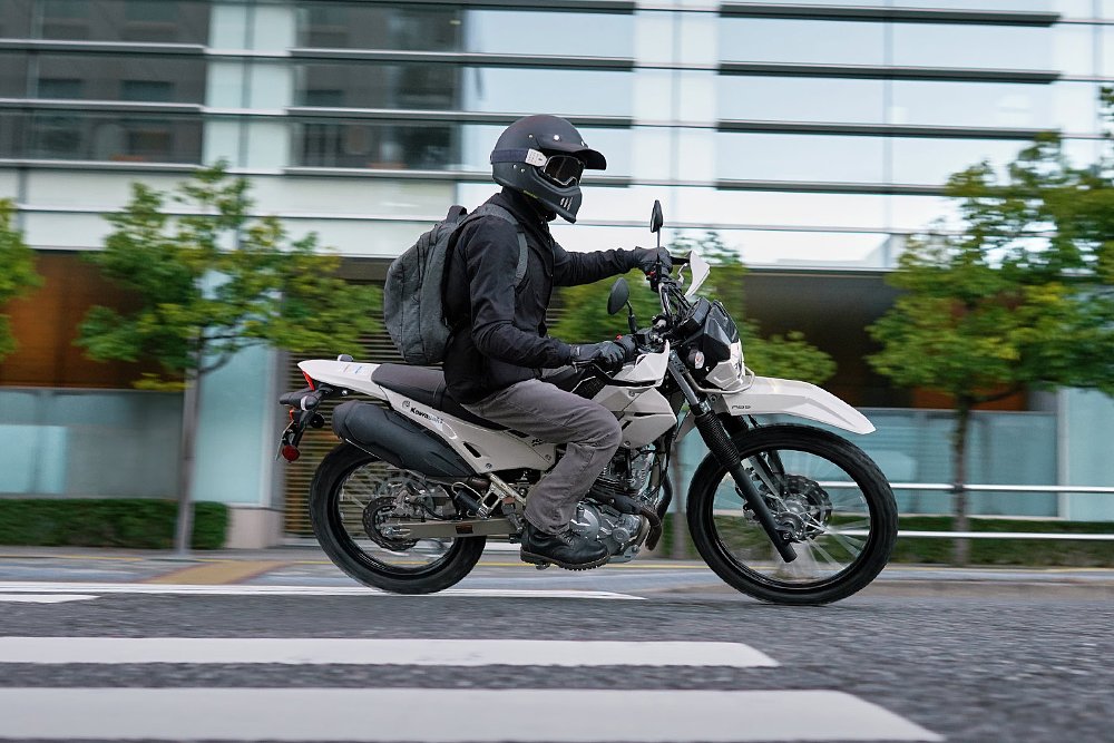 A KLX230 Sherpa S rider riders through an urban landscape.
