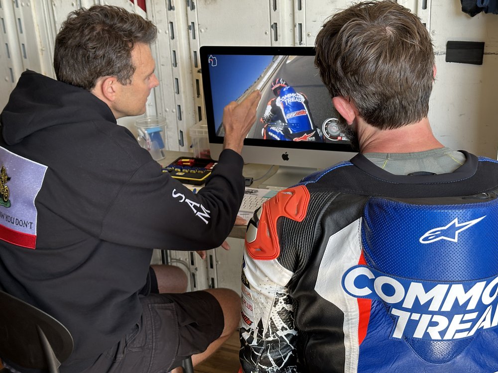 Two people analyze on-board footage of a motorcycle riding around a track.