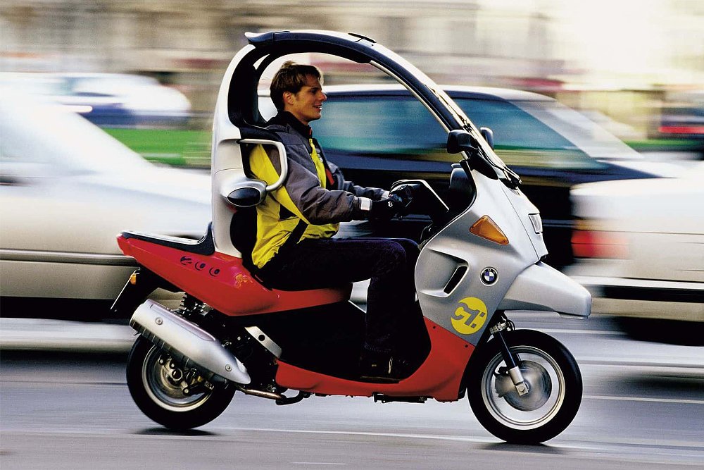 우연히 옷을 입은 라이더는 도시 경관을 통해 BMW C1 폐쇄 스쿠터를 운영합니다.