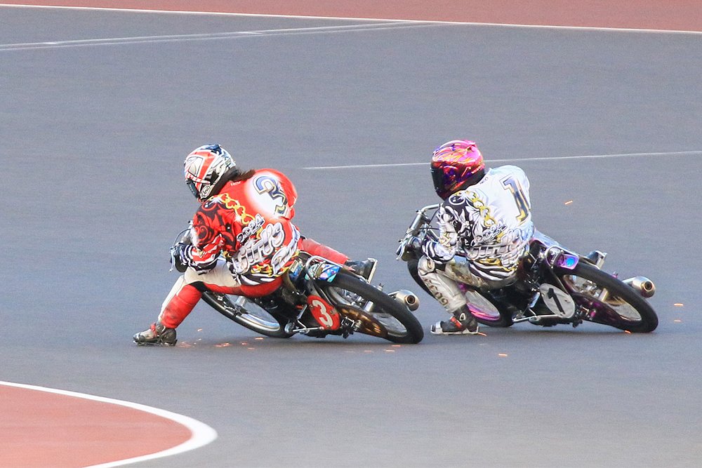 Two auto racers speed into a corner with their metal boots shooting up sparks.