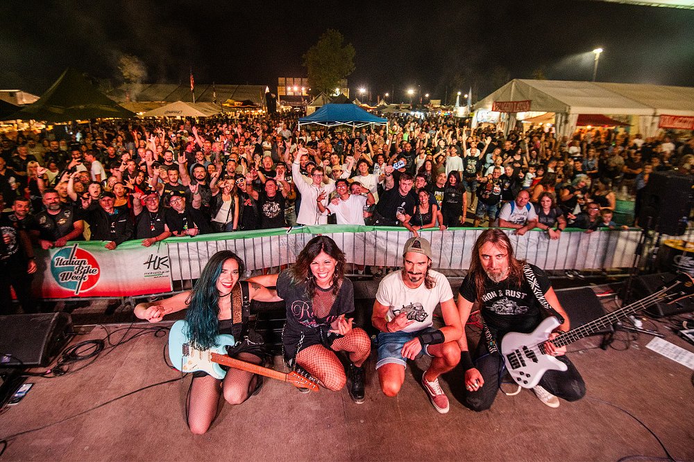 환호하는 팬들을 배경으로 밴드가 카메라를 향해 포즈를 취하고 있다.