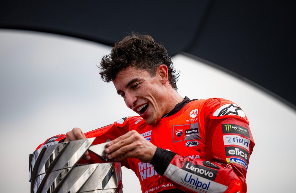 smiling Marc Marquez adds the silver plaque with his name to the MotoGP trophy