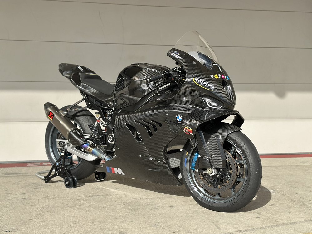 2025 alpha Racing M 1000 RR posed in front of a garage door at a racetrack.