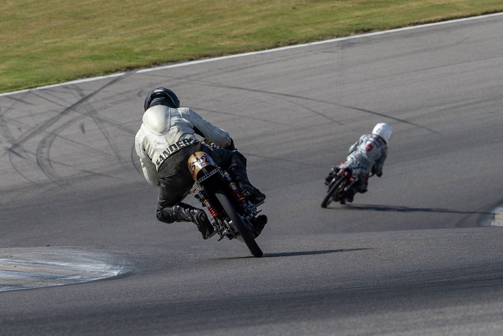 two racers banking through the curves on the track, seen from behind, on very old vintage motorcycles
