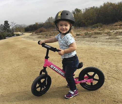 smiling girl on a Strider bike on a dirt path