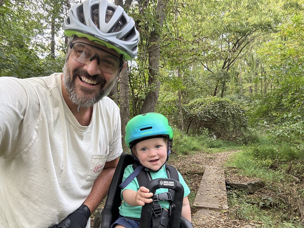 Spurgeon and his son smiling on the bicycle trail with the boy in the Shotgun Pro seat