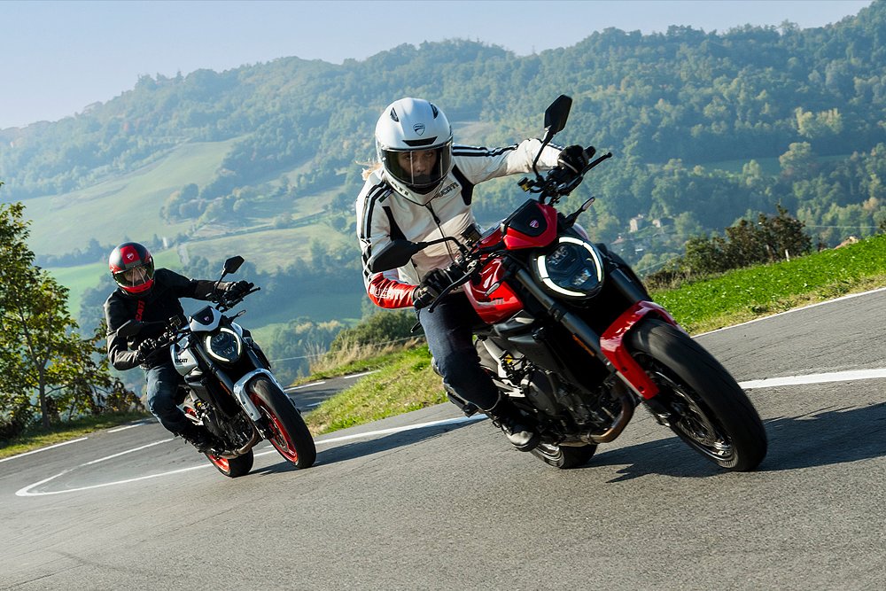 Two Ducati Monster+ riders attack corners on a mountain road.