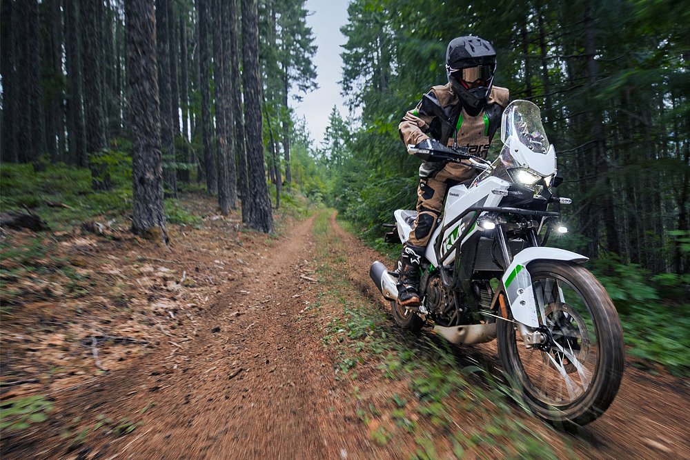 A KLE500 rider attacks a tree-lined mountain trail.