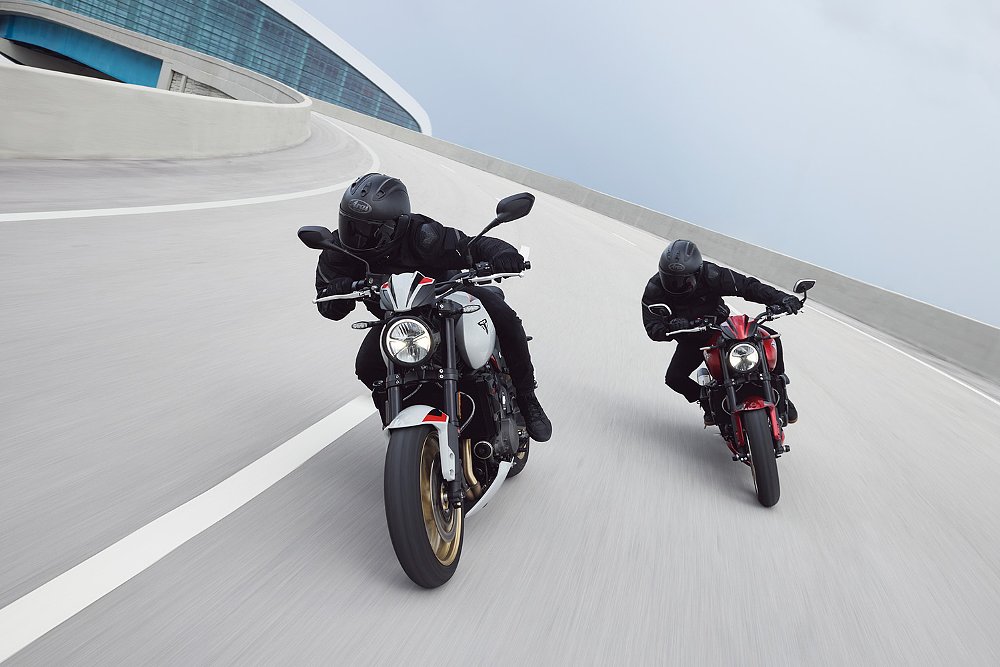 Two Trident 800 riders speed around a curve on an urban overpass.